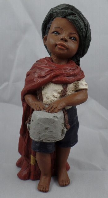 A child-like statue holding a gray bag, wearing a red scarf and casual clothes.