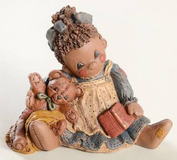 A vintage doll reading a book with two smaller dolls beside her.